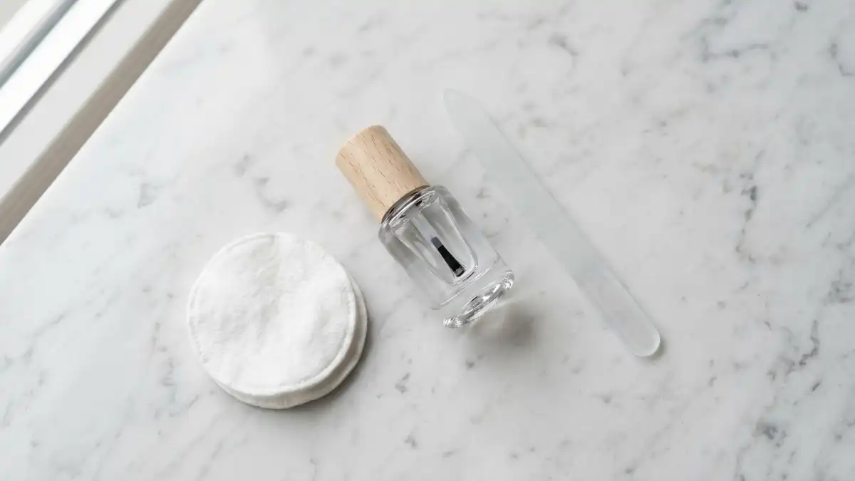 Nagelpilz-Lösung mit Pinselapplikator, Glasfeile und Wattepads auf Marmor
